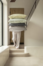 Person trägt vier gestreifte Kissen in verschiedenen Farben eine Treppe hinauf, seitliche Perspektive