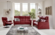 Modernes Wohnzimmer mit einem roten 2er-Sofa aus Leder, frontal betrachtet, umgeben von großen Fenstern, einem Sessel und einem Couchtisch.