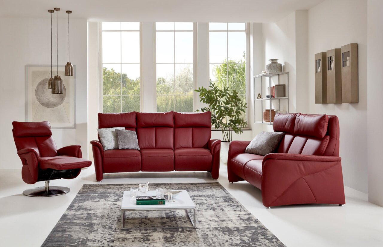 Modernes Wohnzimmer mit einem roten 2er-Sofa aus Leder, frontal betrachtet, umgeben von großen Fenstern, einem Sessel und einem Couchtisch.