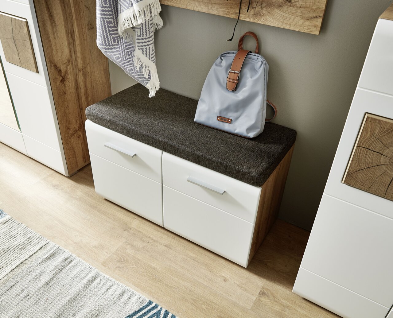 Moderne Bank mit weißem Korpus und dunklem Sitzpolster, seitliche Perspektive, mit Rucksack darauf.