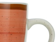 Detailaufnahme einer gesprenkelten Keramiktasse in Terrakotta-Orange mit braunem Rand und weißem Henkel, Seitenansicht vor weißem Hintergrund