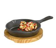 Gusseiserne Grillpfanne mit Griff, gefüllt mit Garnelen und Chilischoten, auf einem runden Holzbrett, seitliche Perspektive