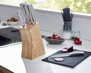 Messerblock aus Holz mit sechs Edelstahlmessern, auf einer Küchenarbeitsplatte platziert, mit einem geschnittenen Messer und Zwiebeln im Vordergrund. Perspektive von der Seite.