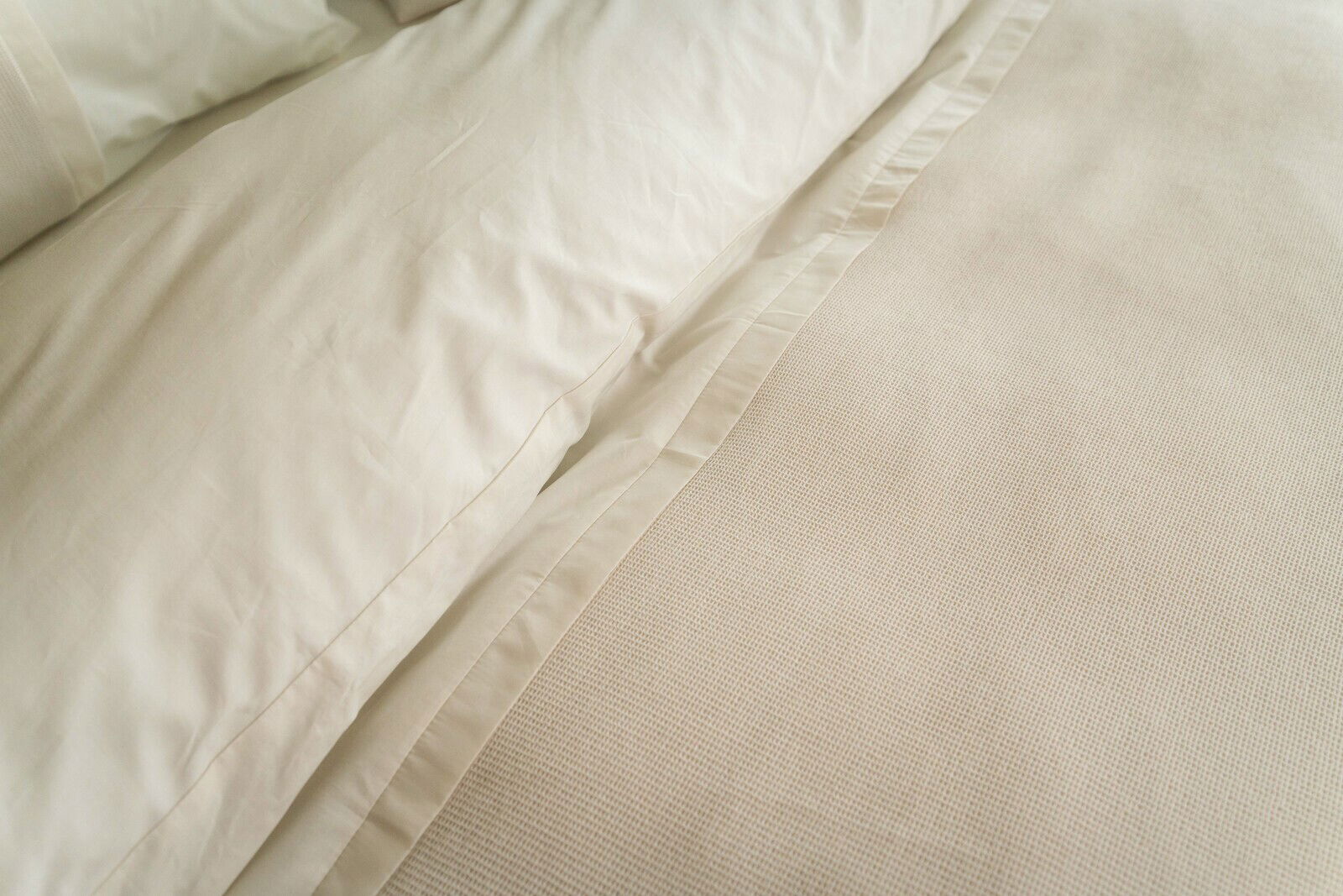 Nahaufnahme von cremefarbener Bettwäsche mit Kissenbezug und Decke in einer strukturierten Stoffoptik.
