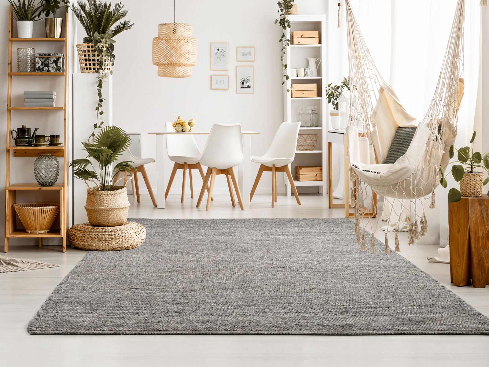 Grauer Handweb Teppich in modernem Wohnzimmer mit Pflanzen und Hängesessel, aus der Perspektive des Raumes fotografiert.
