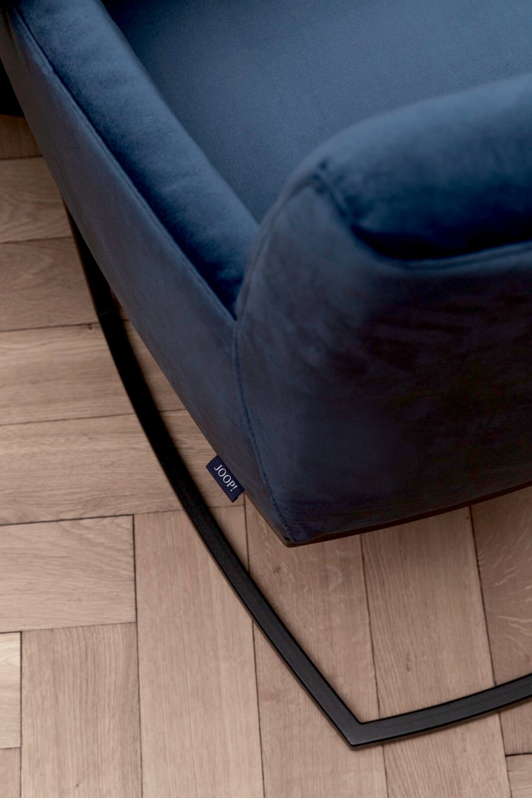 Nahaufnahme eines blauen Freischwinger-Sessels mit schwarzem Metallgestell auf Holzboden, von oben betrachtet.