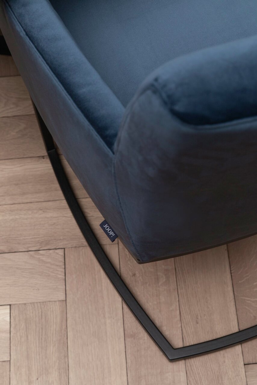 Close-up van een blauwe zweefstoel met een zwart metalen frame op een houten vloer, gezien van bovenaf.