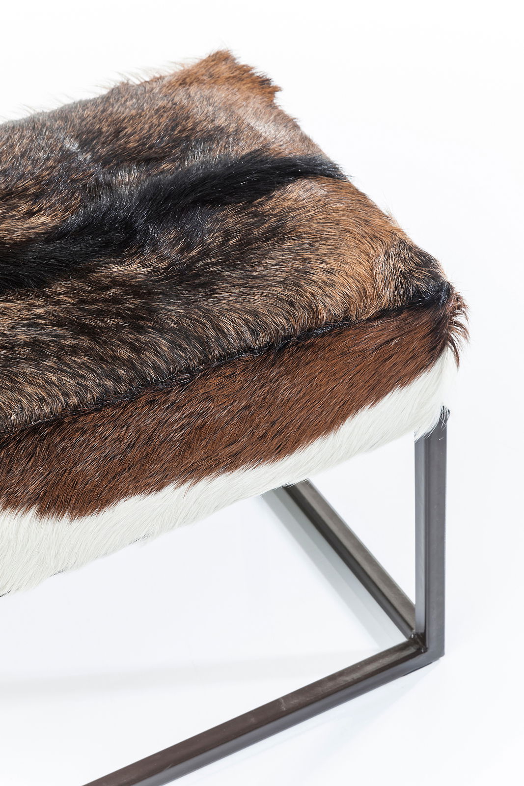 Nahaufnahme einer Bank mit einem Sitz aus braunem, schwarzem und weißem Fell, gestützt von einem Metallrahmen. Perspektive von schräg oben.