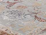 Nahaufnahme eines Orientteppichs mit floralen Mustern in Rot, Blau und Beige auf grauem Hintergrund, von schräg oben fotografiert.