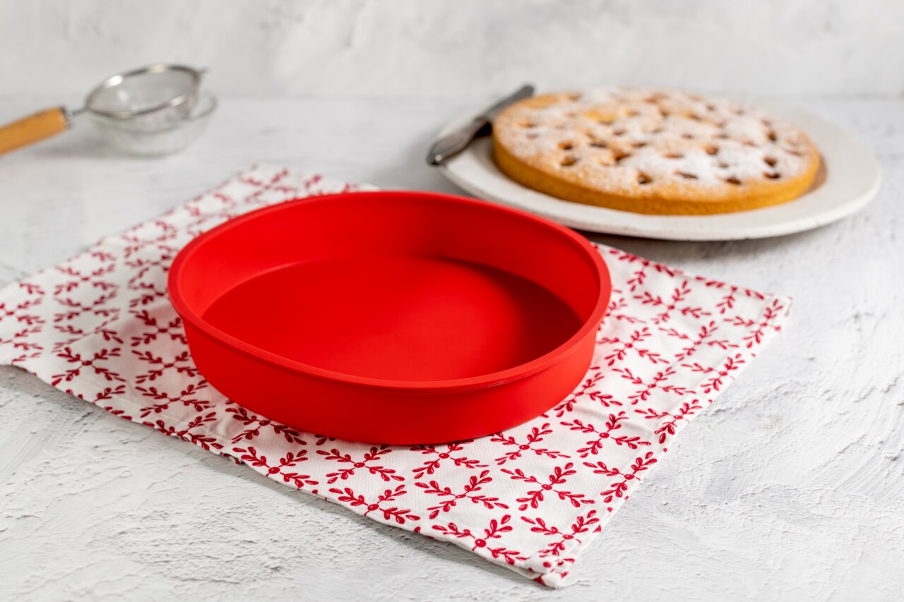 Dr. Oetker Silikon-Rundform FLEXXIBEL Rote Silikon-Rundform mit einem Durchmesser von 26 cm, auf einem dekorativen Tuch in der Küche platziert, seitliche Perspektive.