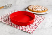 Rote Silikon-Rundform mit einem Durchmesser von 26 cm, auf einem dekorativen Tuch in der Küche platziert, seitliche Perspektive.