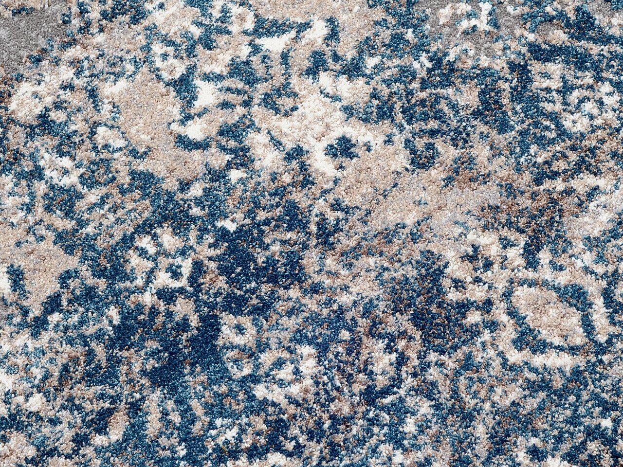 Nahaufnahme eines Designer-Teppichs mit abstraktem Muster in Blau- und Beigetönen, von oben betrachtet.