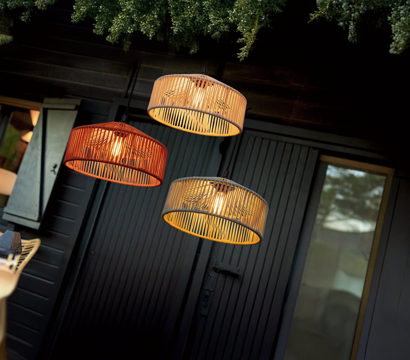 Drei runde Pendelleuchten mit Bambus-/Rattan-Lampenschirmen in Natur- und Orangeton, warm leuchtend, hängend vor dunkler Holzverkleidung; Perspektive: leicht von unten und schräg aufgenommen.