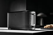 Schwarzer Langschlitztoaster in seitlicher Perspektive auf einer Küchenarbeitsplatte, mit mehreren Bedienelementen und einem eleganten, modernen Design.