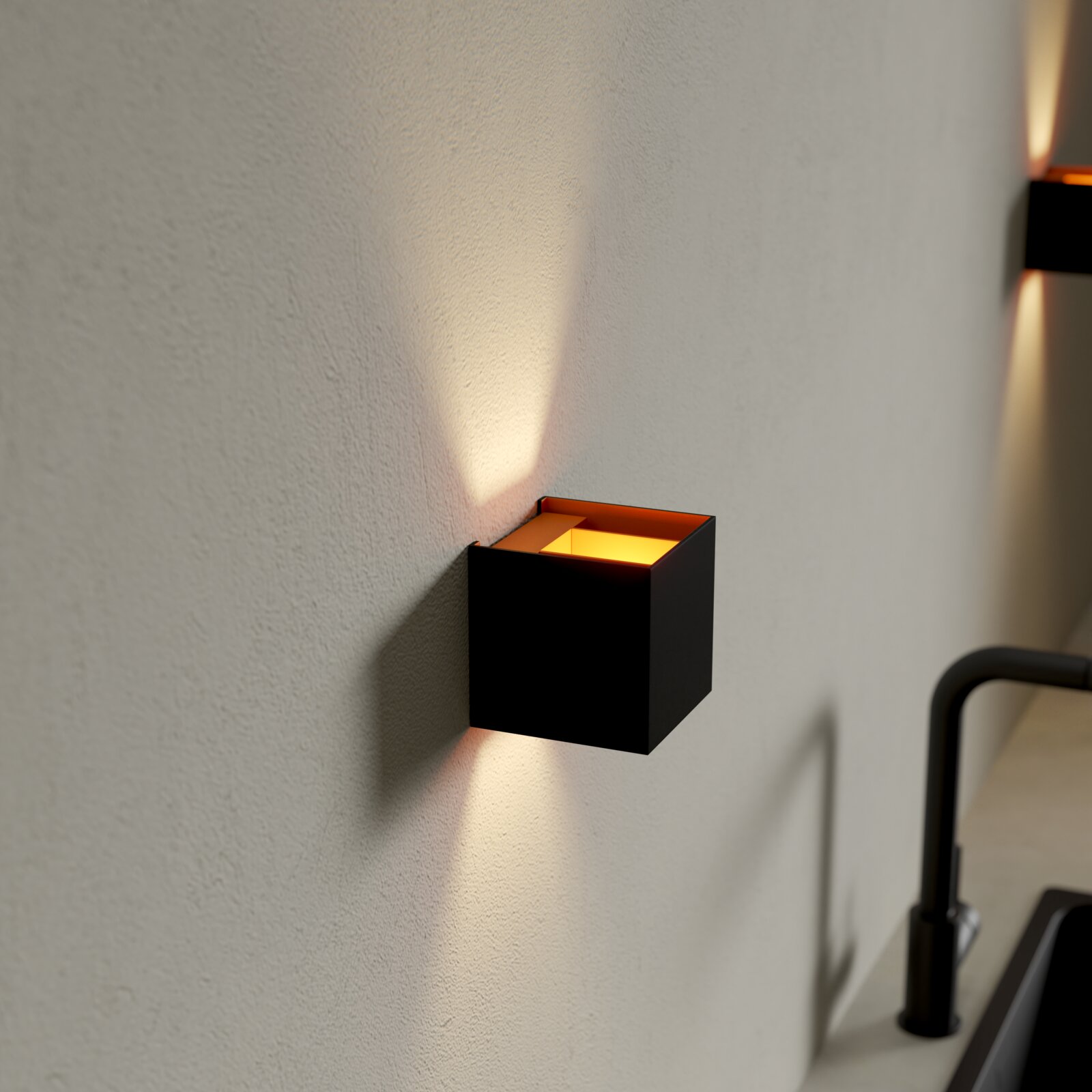 Schwarze, würfelförmige Wandleuchte mit warmweißem Up-&-Down-Lichtkegel an heller Wand, Perspektive: seitliche Nahaufnahme leicht von vorn