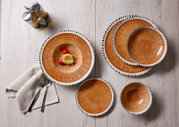 Bovenaanzicht van een rustiek servies met bruine kommen en borden, voorzien van een crèmekleurige rand met zwarte accenten, stijlvol gedekt op een lichte houten tafel.