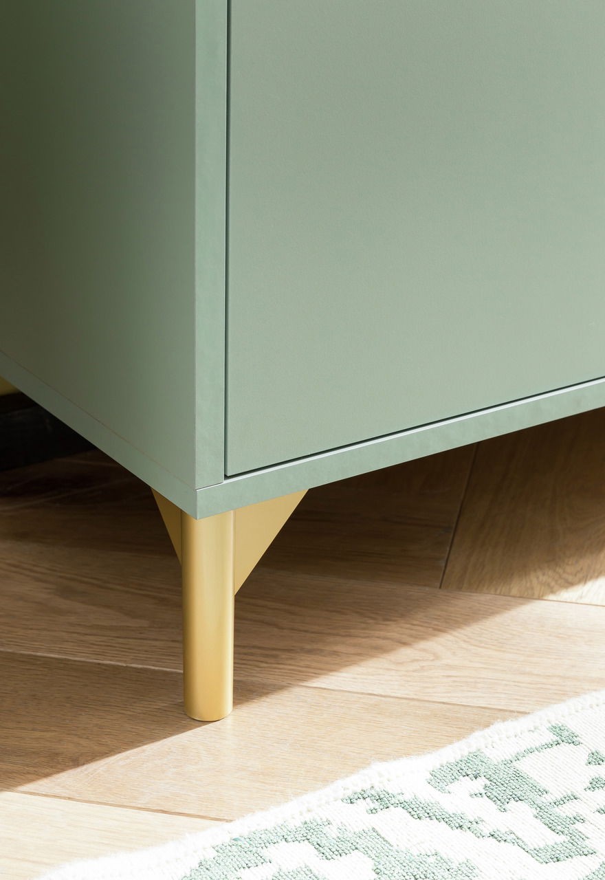 Nahaufnahme eines grünen Highboards mit goldenen Beinen, von der Seite fotografiert.