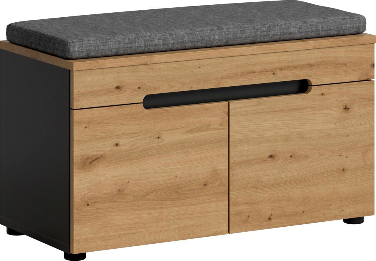 Schuhbank mit grauem Sitzpolster, Holzoptik-Front und schwarzen Seitenteilen, zwei Klappenfächer mit Griffmulde, Ansicht schräg von vorne.