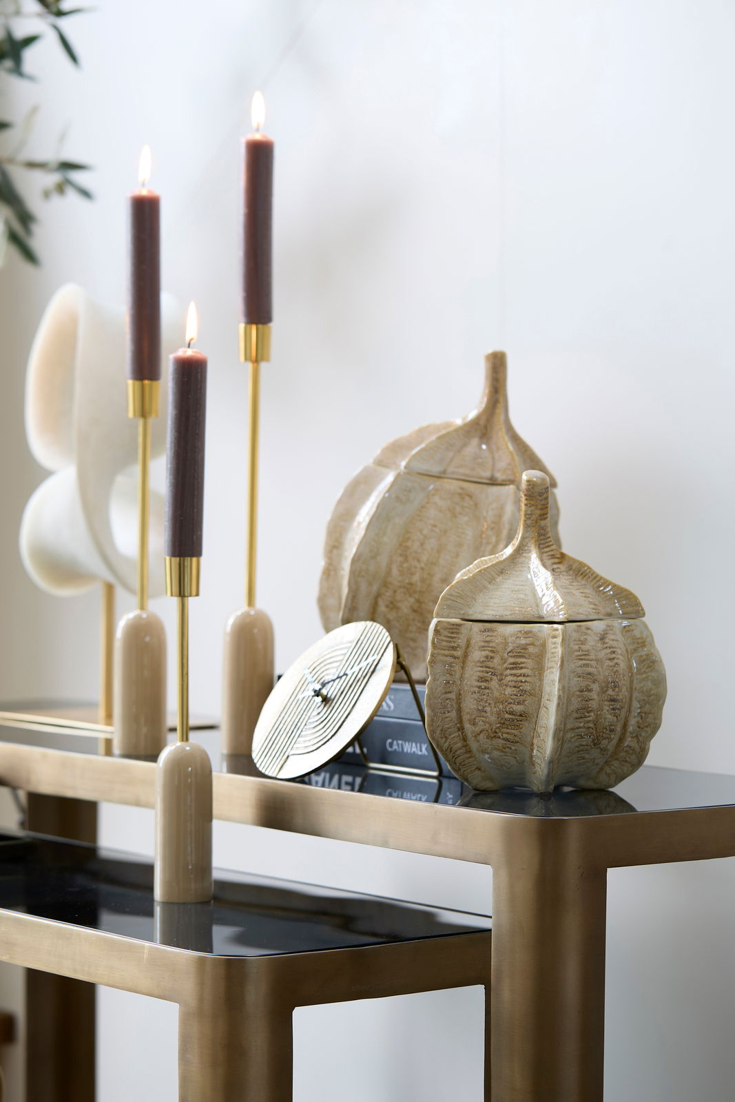 Dekorative Box in Form eines Kürbisses auf einem Tisch, umgeben von eleganten Kerzenhaltern und Büchern, seitliche Perspektive.