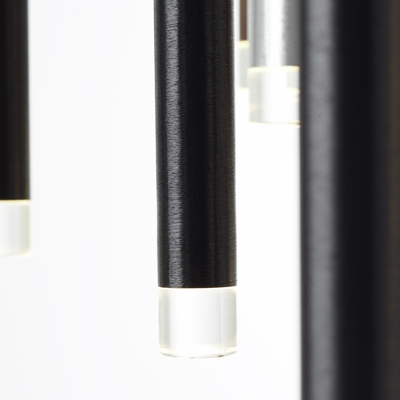 Nahaufnahme von hängenden, zylindrischen LED-Leuchten mit schwarzem Gehäuse und transparentem Ende, seitliche Perspektive