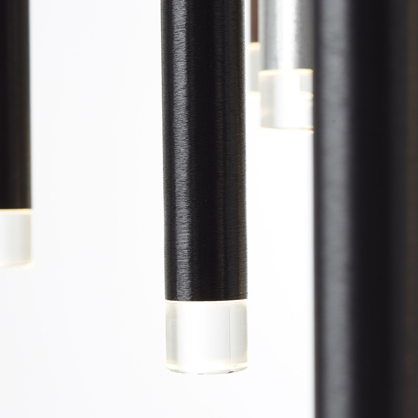 Nahaufnahme von hängenden, zylindrischen LED-Leuchten mit schwarzem Gehäuse und transparentem Ende, seitliche Perspektive