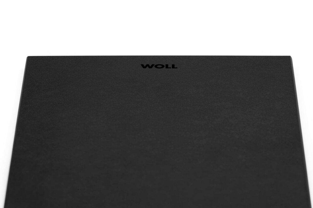 Close-up van een zwart rechthoekig ontbijtbord met het logo 'WOLL' in het midden.