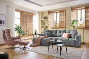 Gemütliche Wohnzimmer-Ecke mit grauem Ecksofa, rosa Sessel und Hocker, sowie modernen Holzmöbeln und Pflanzen. Perspektive von vorne.