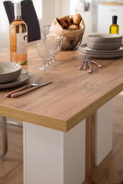 Nahaufnahme eines Esstisches mit Holzoberfläche, gedeckt mit Geschirr, Besteck, einer Flasche Wein und einem Brotkorb.