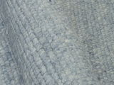 Nahaufnahme eines handgewebten Teppichs in graublauer Farbe mit strukturierter Oberfläche, seitliche Perspektive