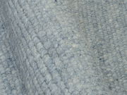 Nahaufnahme eines handgewebten Teppichs in graublauer Farbe mit strukturierter Oberfläche, seitliche Perspektive