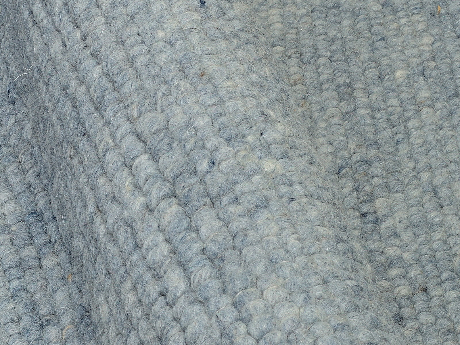 Nahaufnahme eines handgewebten Teppichs in graublauer Farbe mit strukturierter Oberfläche, seitliche Perspektive