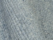Nahaufnahme eines handgewebten Teppichs in graublauer Farbe mit strukturierter Oberfläche, seitliche Perspektive