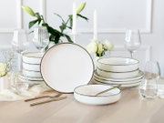 Elegantes weißes Porzellan-Geschirrset mit feinem Goldrand, Teller und Schalen auf gedecktem Tisch mit Gläsern, Kerzen und weißen Blumen, frontal in leichter Schrägansicht aufgenommen