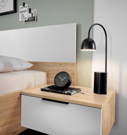 Nachttisch mit Holz- und Weiß-Design, darauf eine schwarze Tischlampe und ein schwarzer Wecker, seitliche Perspektive