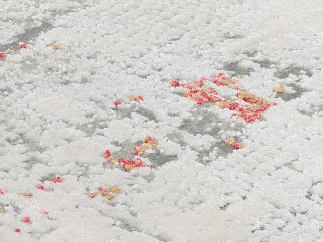 Nahaufnahme eines Designer Teppichs mit weißer, flauschiger Textur und vereinzelten roten und gelben Akzenten. Perspektive von oben.