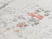 Nahaufnahme eines Designer Teppichs mit weißer, flauschiger Textur und vereinzelten roten und gelben Akzenten. Perspektive von oben.