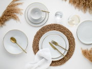Draufsicht auf ein elegant gedecktes Tischarrangement mit weißem Porzellan-Geschirr mit Goldrand, goldfarbenem Besteck, geflochtenem Platzset, Wasserglas und Weißweinglas auf hellem Hintergrund, dekoriert mit Trockengras.