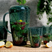 Grünes Kannenset mit Bechern, gefüllt mit Wasser, Himbeeren und Minzblättern, auf einem Tisch mit Apfelstücken, seitliche Perspektive.