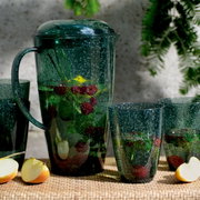 Grünes Kannenset mit Bechern, gefüllt mit Wasser, Himbeeren und Minzblättern, auf einem Tisch mit Apfelstücken, seitliche Perspektive.