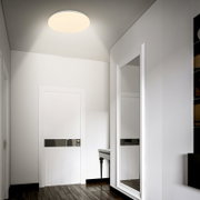 Ronde plafondlamp met warme, diffuse verlichting in een moderne hal met witte deuren en een grote spiegel, gezien vanuit een laag standpunt omhoog richting het plafond