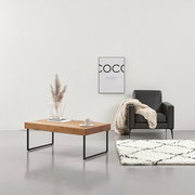 Moderner Couchtisch aus Holz mit Metallbeinen, seitliche Perspektive, dekoriert mit Vase und Tasse, neben einem schwarzen Sessel und einem cremefarbenen Teppich.