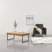 Moderner Couchtisch aus Holz mit Metallbeinen, seitliche Perspektive, dekoriert mit Vase und Tasse, neben einem schwarzen Sessel und einem cremefarbenen Teppich.