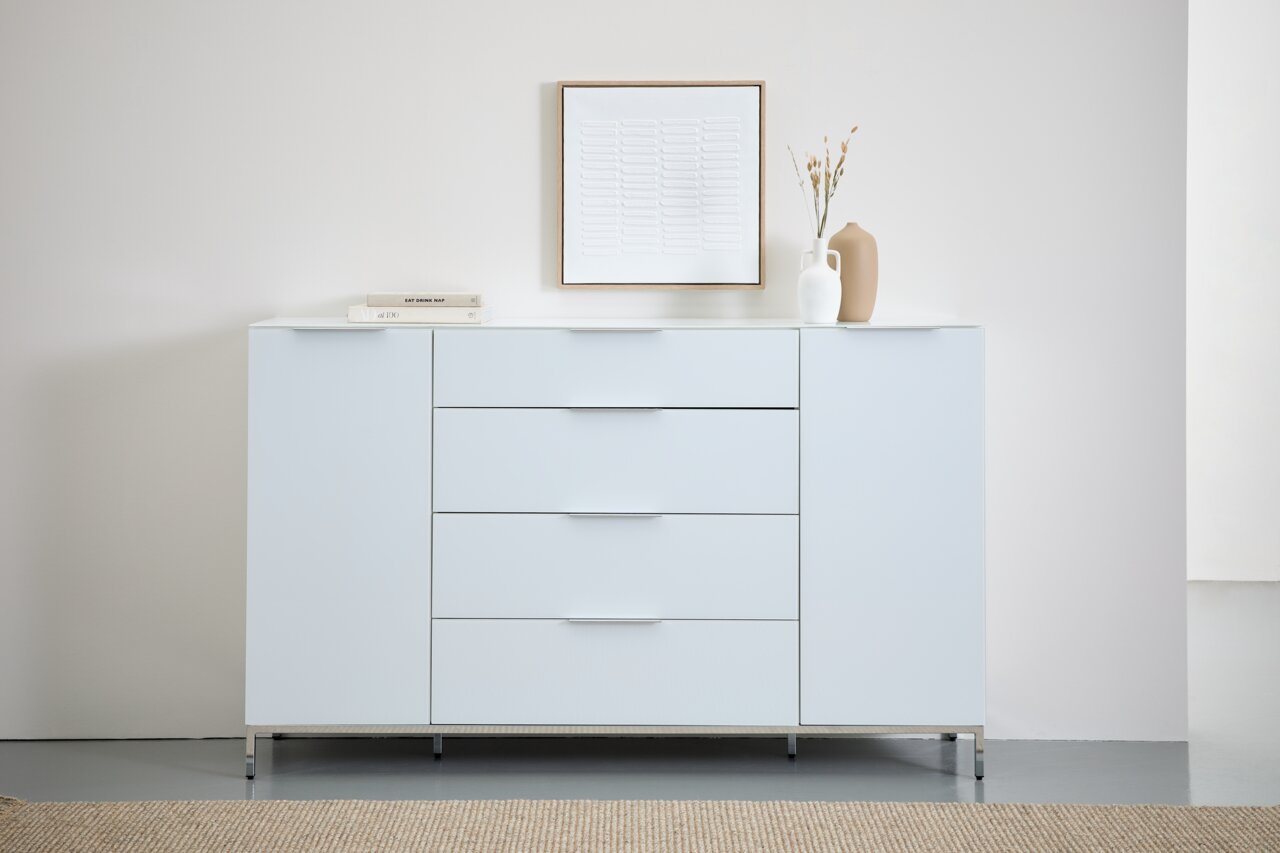 Modernes weißes Sideboard mit vier Schubladen und zwei Türen, dekoriert mit Büchern und Vasen, aus frontaler Perspektive.