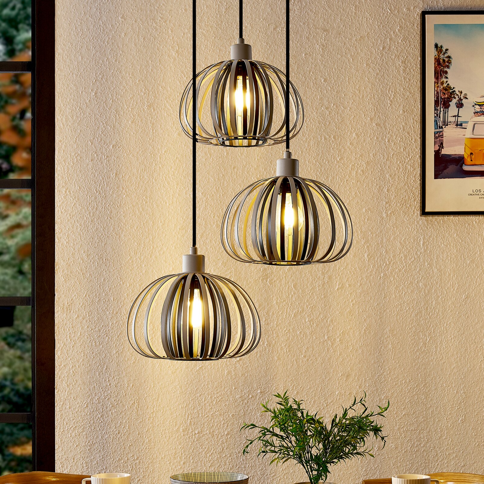 Drie moderne hanglampen met metalen, bolvormige kappen die aan het plafond hangen. Op de foto zijn de lampen van opzij te zien in een gezellige ruimte.