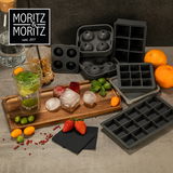 Verschiedene Eiswürfelformen aus Silikon in verschiedenen Größen und Formen, präsentiert auf einem Tisch mit frischen Früchten und Getränken. Perspektive von oben.