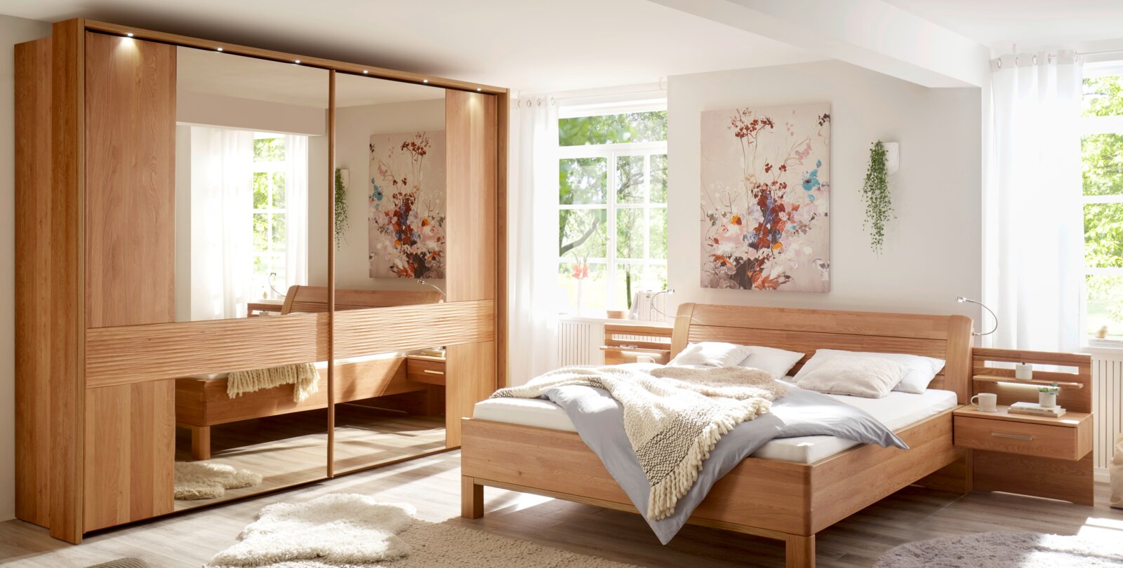 Helles Schlafzimmer mit modernem Massivholz-Bett und passendem Kleiderschrank mit großen Spiegeltüren, fotografiert aus leicht schräger Frontansicht.