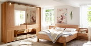 Helles Schlafzimmer mit modernem Massivholz-Bett und passendem Kleiderschrank mit großen Spiegeltüren, fotografiert aus leicht schräger Frontansicht.