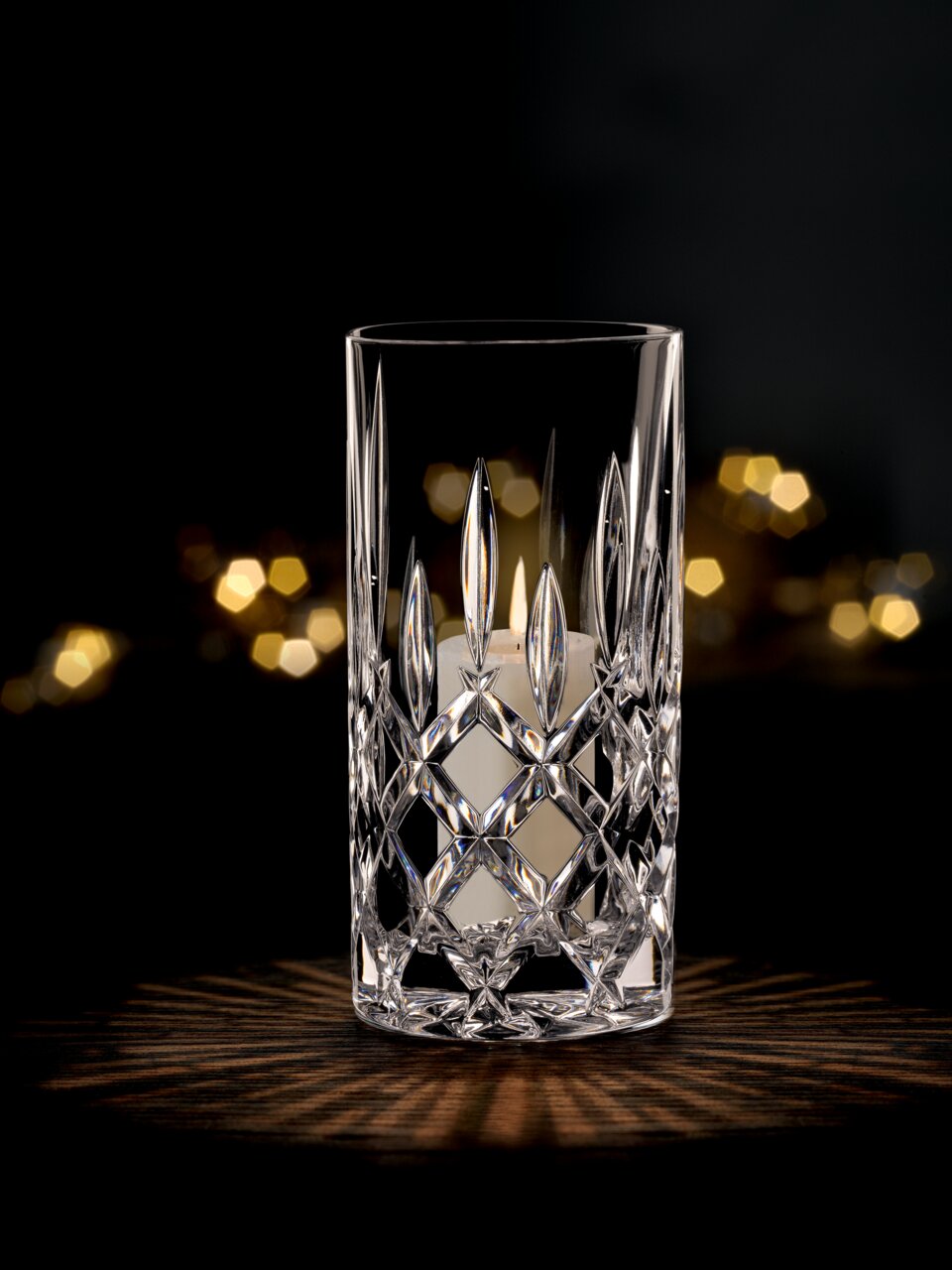 Kristallklare Vase oder Windlicht mit elegantem Schliffmuster, frontal fotografiert, vor einem dunklen Hintergrund mit warmen Lichteffekten.