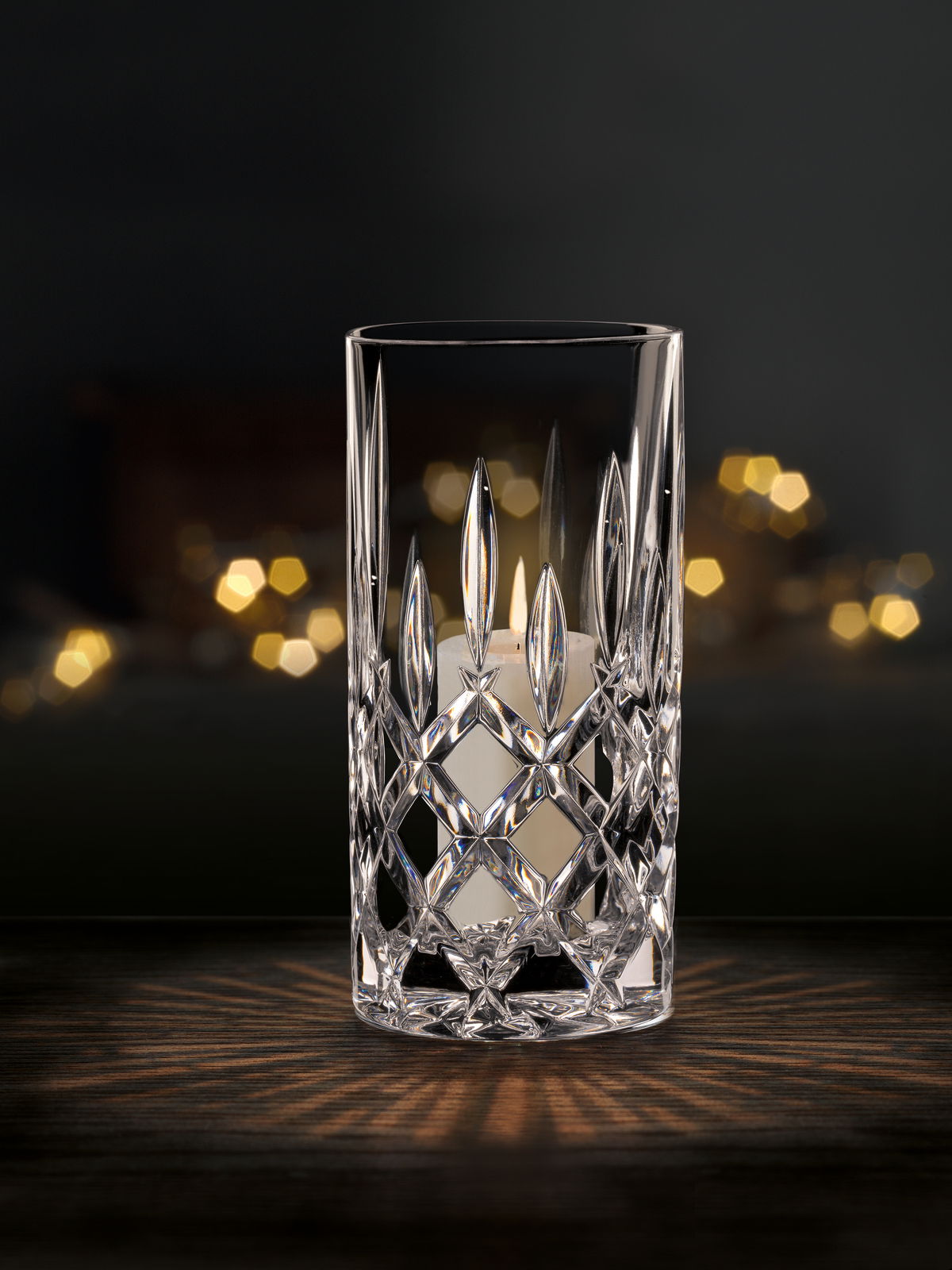 Kristallklare Vase oder Windlicht mit elegantem Schliffmuster, frontal fotografiert, vor einem dunklen Hintergrund mit warmen Lichteffekten.