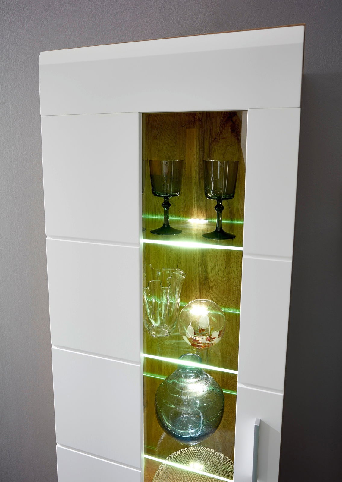 Detailansicht einer modernen Wandkombination mit Glastüren und LED-Beleuchtung, die Gläser und Dekorationsobjekte präsentiert.